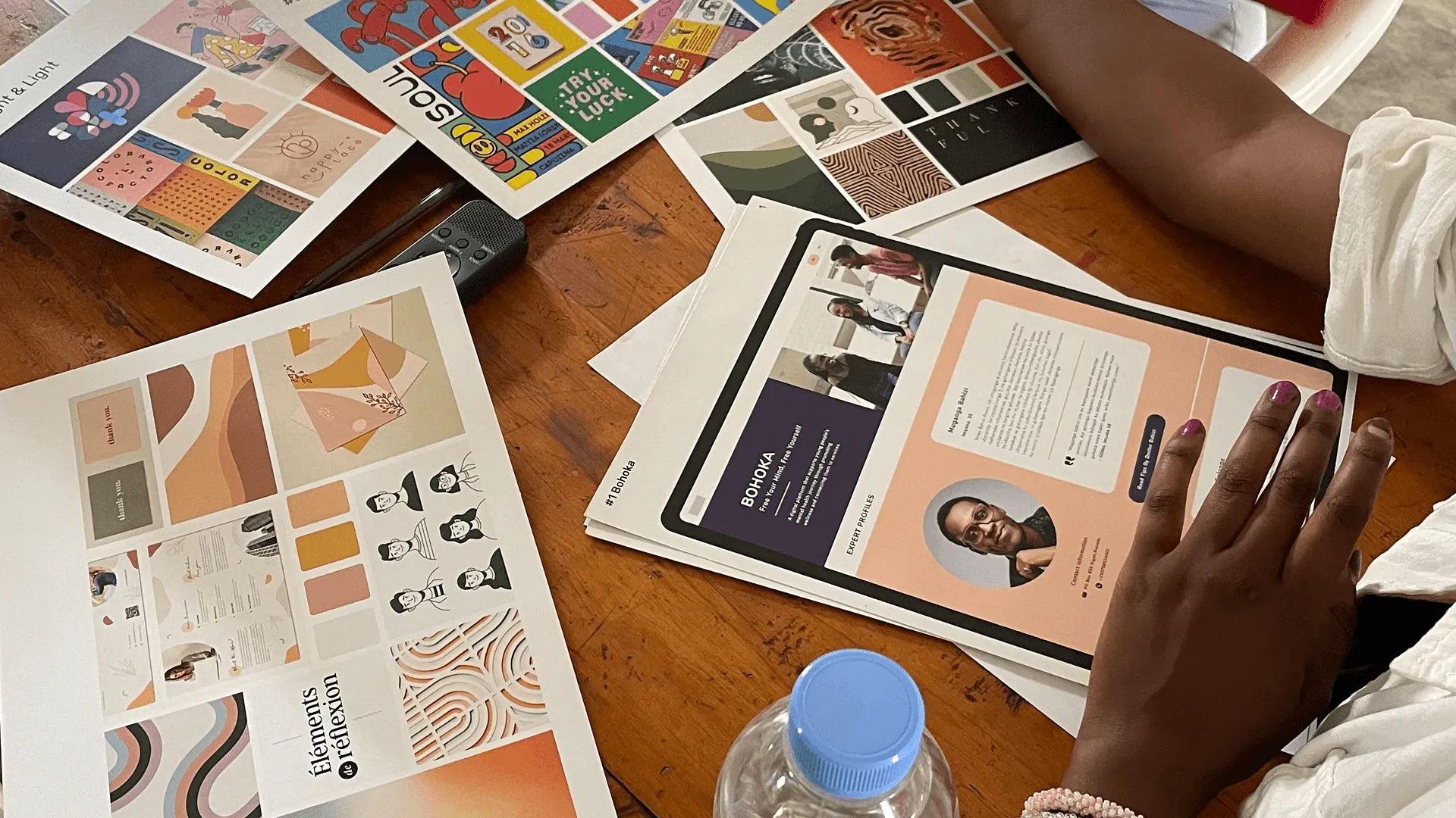 Printed design boards, colour palettes and a Bohoka web page mock-up laid out on a wooden table during a workshop.